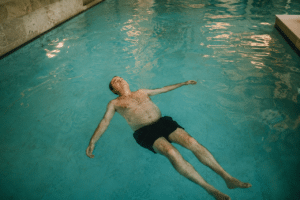 Adulto flotando de espaldas en pileta climatizada, expresión serena de relajación y confianza con el agua