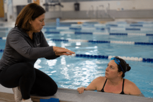 Profesor de natación enseñando técnica a alumna adulta junto al borde de la pileta