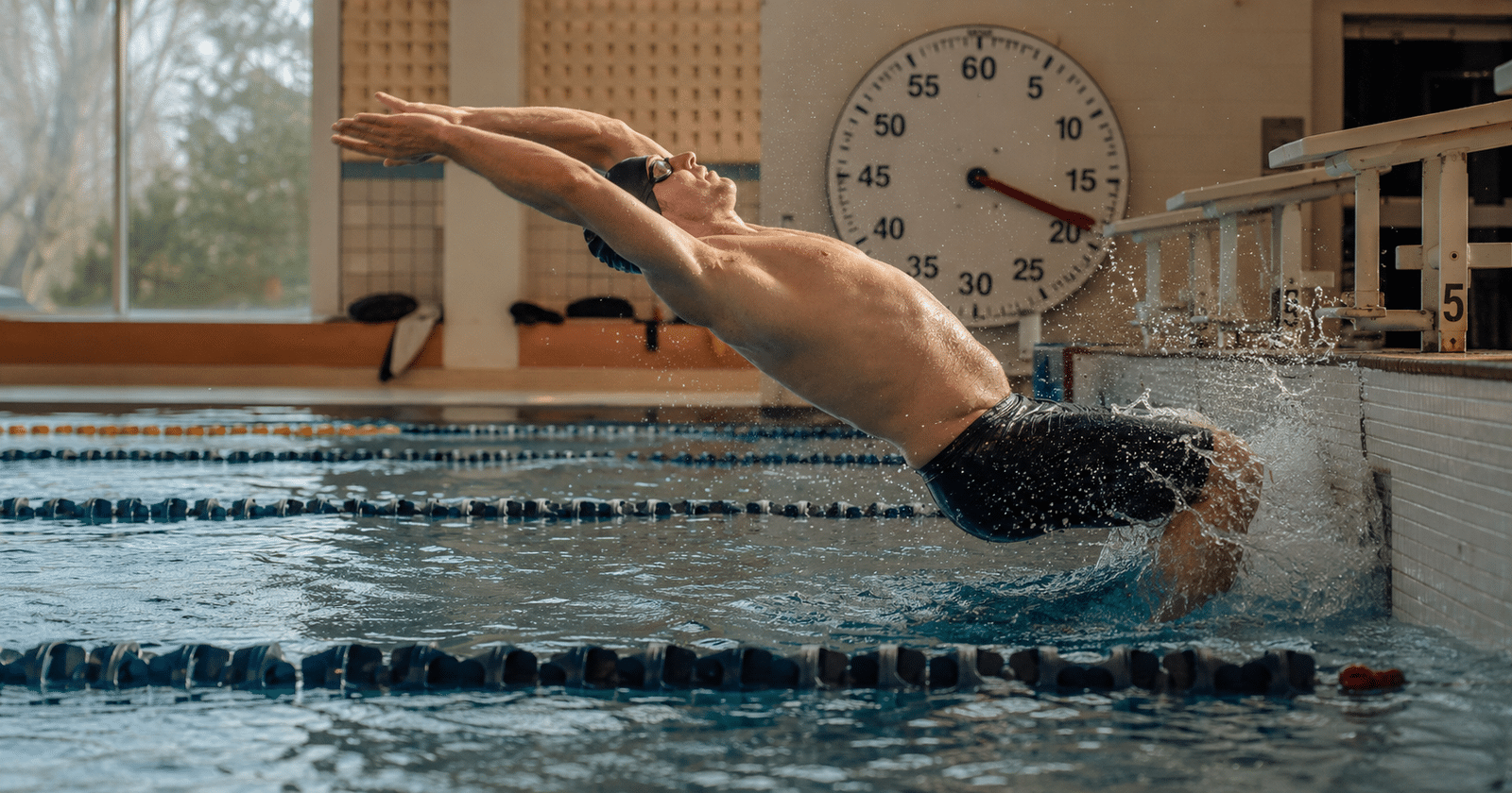 Nadador iniciando una serie de natación con reloj de pared visible al fondo